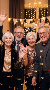 Group of elderly friends celebrating together at a festive party with confetti and decorative lights in a cozy indoor setting