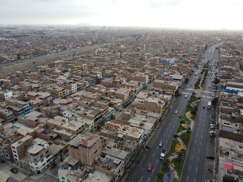 Aerial view of Avenida Peru cutting through the dense residential neighborhood with multi-story buildings and busy traffic in San Martin de Porres, Lima, Peru.