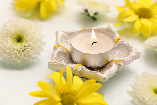 Diya lamp with burning candle and beautiful flowers in water on white background. Divaly celebration