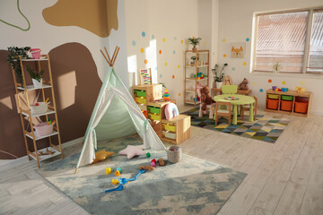Interior of stylish playroom with play tent, toys and shelving unit in kindergarten © Pixel-Shot