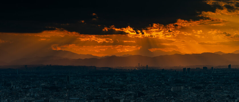Dramatic Tokyo cityscape with powerful sunbeams breaking through stormy sunset clouds over distant mountains