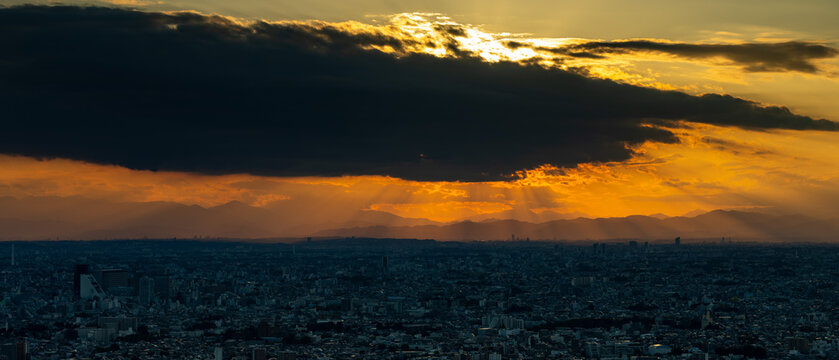 Dramatic Tokyo cityscape with powerful sunbeams breaking through stormy sunset clouds over distant mountains
