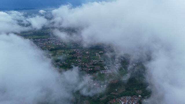 Aerial view of lush green landscape with scattered settlements, agricultural fields, and patches of clouds over the terrain in Sukabumi Regency, West Java, Indonesia.