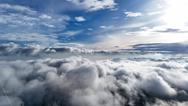 Aerial view of fluffy white clouds under a bright blue sky with sunlight filtering through the atmosphere in Sukabumi Regency, West Java, Indonesia.