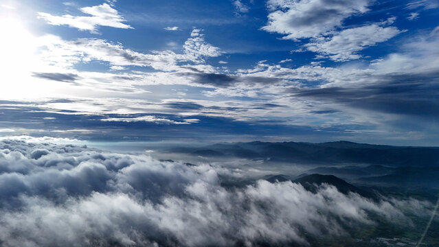 Aerial view of mountainous terrain with rolling hills, dense clouds, and bright sunlight, Sukabumi Regency, West Java, Indonesia.