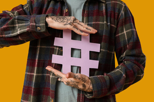 Cool tattooed young man with hashtag symbol on yellow background, closeup