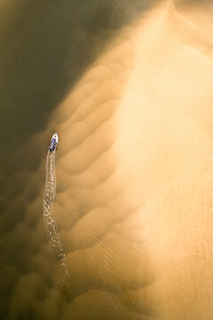 Aerial view of a small boat leaving a wake in the shallow, rippled sandy waters of the Noosa River in Noosa Heads, Queensland, Australia.