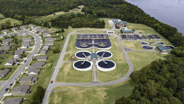 Aerial view of a wastewater treatment plant with circular tanks, adjacent to a residential neighborhood with suburban houses, surrounded by trees in Gallatin, Tennessee, United States.