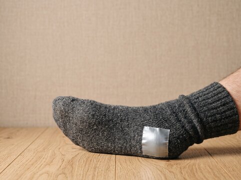 Grey wool sock with duct tape patch on a wooden floor surface