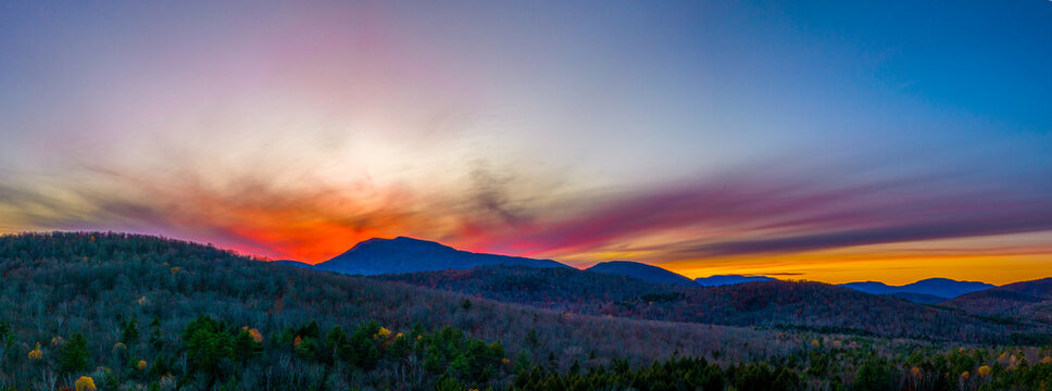 Aerial view of a vibrant sunset over the Adirondack Mountains with colorful clouds and autumn foliage covering the rolling hills in Warrensburg, New York, United States.