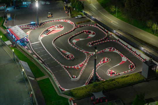Aerial view of an illuminated go-kart track at night with red and white safety barriers and asphalt curves in Poland.