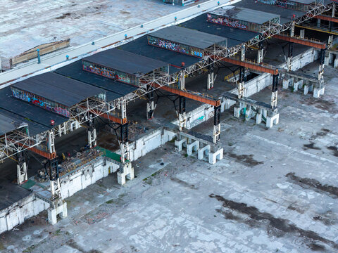 Aerial view of an industrial warehouse featuring weathered roofs with graffiti, exposed steel support beams, and a large concrete yard in Poland.