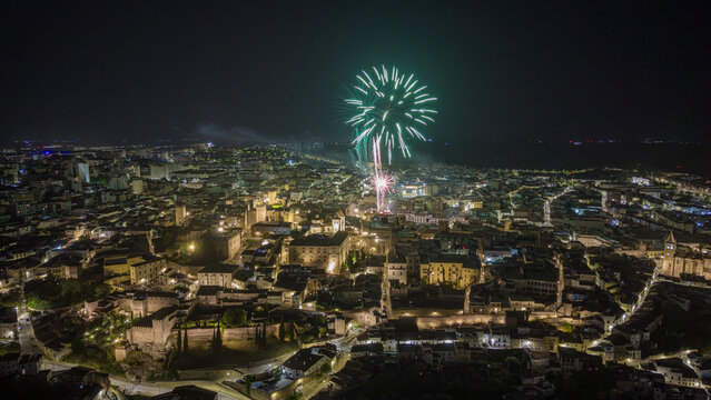 Aerial view of the historic old town of Caceres at night with a green firework exploding over illuminated medieval stone buildings and towers in Caceres, Extremadura, Spain.