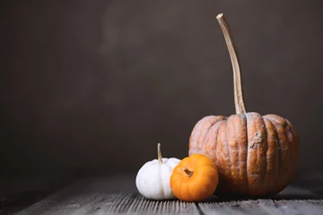 Close-up of three assorted pumpkins on wooden table against dark background in autumn setup. Moody food photography with seasonal styling and rustic fall atmosphere © Ivan Kmit