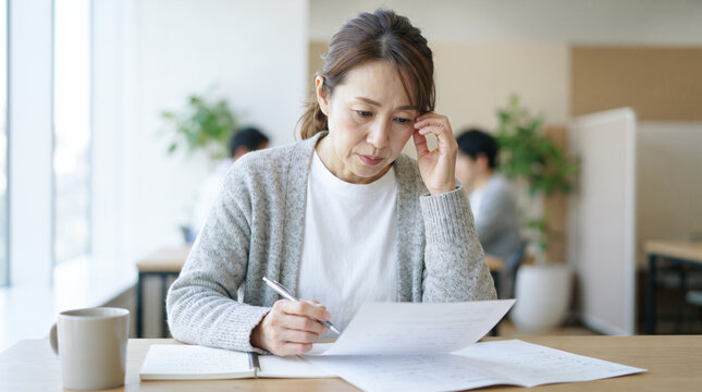 オフィスで書類を見つめて悩むミドル世代の女性会社員
