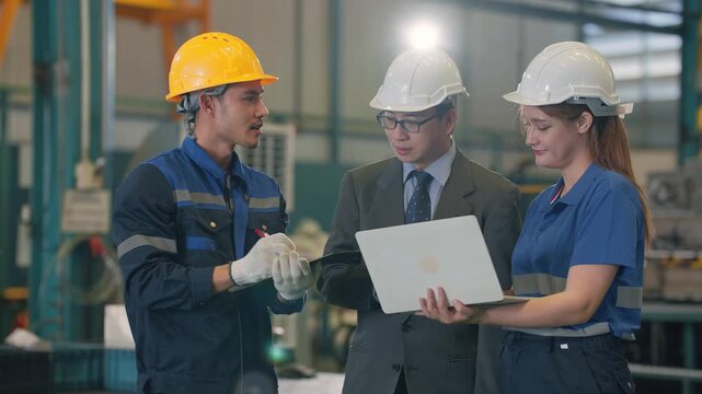 Three professionals inspect machinery in a factory setting. One points upward, indicating a problem or feature. The others observe intently