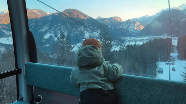 Young child riding a cable car at Almenwelt Lofer in Austria, looking at snowy Alpine mountains through the window during sunset. Cozy winter family travel scene in the Austrian Alps