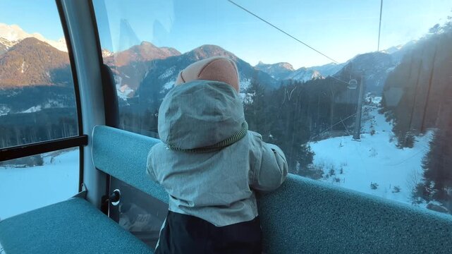 Young child riding a cable car at Almenwelt Lofer in Austria, looking at snowy Alpine mountains through the window during sunset. Cozy winter family travel scene in the Austrian Alps