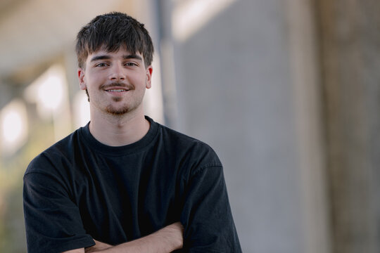 Portrait of a smiling young Caucasian man, confident expression, arms crossed, standing outdoors in natural light