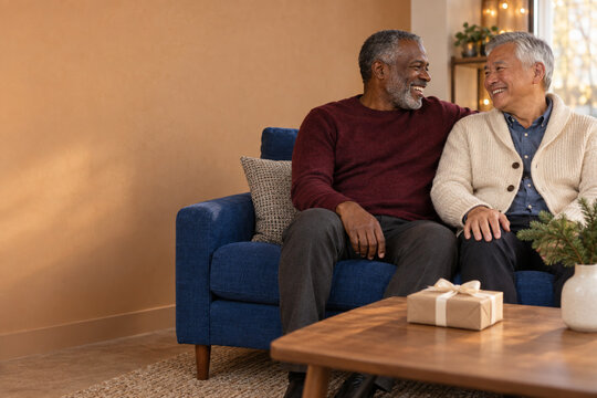 Mature male couple relaxing at home with holiday gift and copy space