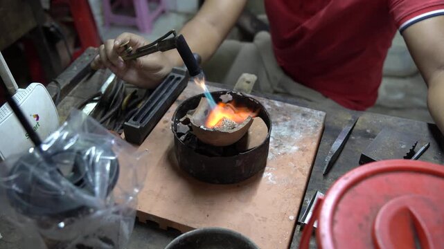 Jewelry maker working with a blowtorch to melt precious metal in a crucible for casting