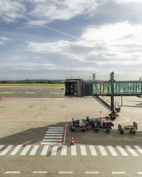 Gdansk, Wojewodztwo pomorskie, Poland - 07 September 2026: View of Gdansk Lech Walesa Airport with a jet bridge over the tarmac and luggage carts parked nearby under a cloudy sky.