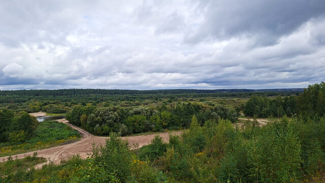 Expansive forest landscape under dramatic cloudy sky with winding dirt road