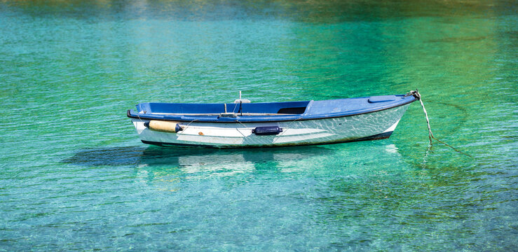 Blue fishing boat moored in the vivid turquoise-green waters of Stari Trogir Bay near Sevid, Croatia, surrounded by sunlit ripples and a visible seabed