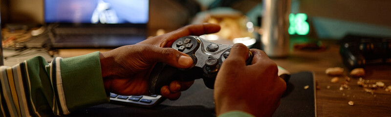 African American young adult man holding gamepad controller while playing video games at computer desk. Visual concept representing digital addiction and esports gaming entertainment © Seventyfour