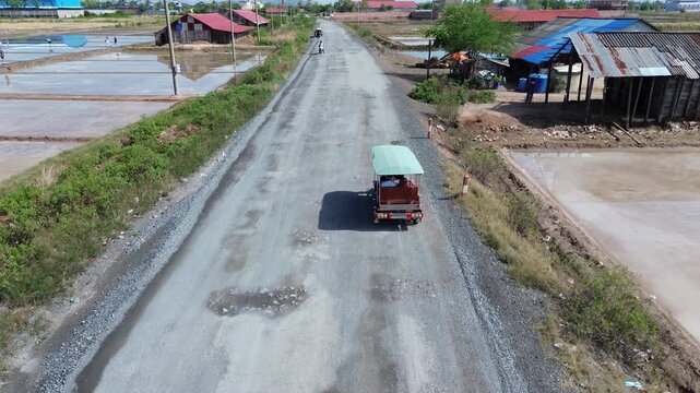 Aerial perspective following a three-wheeled vehicle driving on a bumpy rural road near salt fields