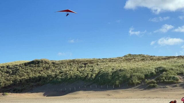 Paraglider fliegt &uuml;ber D&uuml;nen am Strand an einem warmen Sommertag mit blauem Himmel