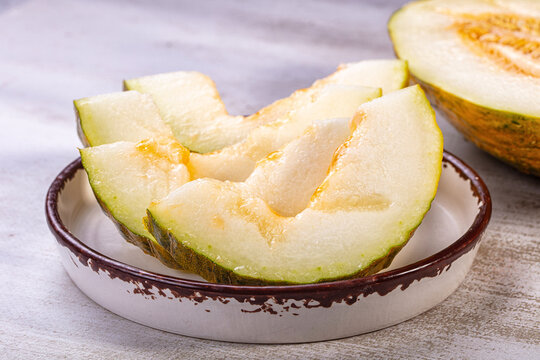 Sliced piel de sapo melon wedges on rustic ceramic plate, pale green flesh with golden center, shallow depth of field, natural light