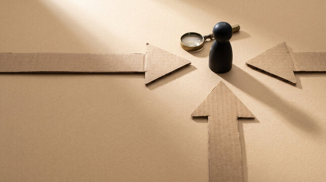 Cardboard arrows converging on wooden figure with magnifying glass