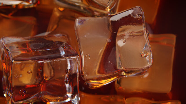 A closeup view of clear ice cubes floating in a cola beverage