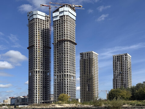 Big hoisting tower cranes in process of dwelling construction of modern high buildings in a city in sunny day