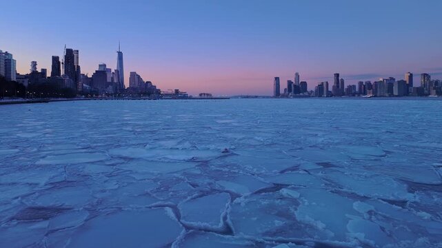 Slow panning view of the Lower Manhattan and Jersey City skylines across the frozen Hudson River, with ice floes covering the water in winter. New York City, USA