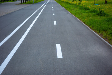 Obraz premium White lane markings on asphalt sidewalk through green park, pedestrian infrastructure, recreation and urban mobility.