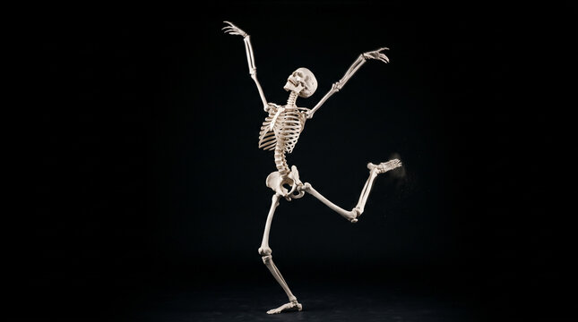 Human skeleton dancing in a dynamic pose against a pure black background, spooky Halloween anatomy concept with dramatic movement and copy space.