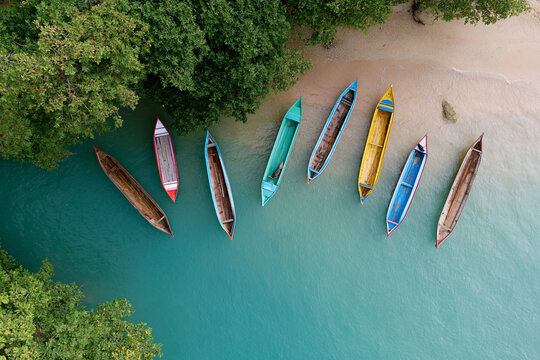 Colorful canoes rest gently on turquoise water. Lush green trees frame the calm shoreline. Sunlight glints softly across the surface. Peaceful stillness suggests a quiet escape