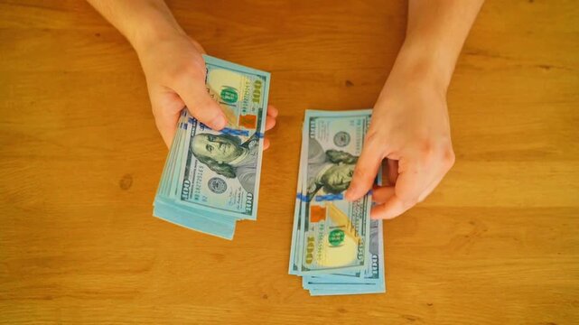 Top view hands counting 100 US dollar bills on wooden table. High angle overhead view of male hands counting stacks of hundred dollar cash notes for business payment,budget planning or finance concept