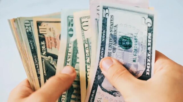 Close up hands holding and sorting mixed US dollar banknotes of different denominations. Person flipping through cash bills including 5, 10, 20, 50, 100 dollars for shopping, payment or budget.