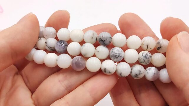 Polished white round gemstone bead strands display natural dendritic inclusions and subtle multi-color mineral patterns across multiple smooth parallel threading strands for artisan jewelry making pro