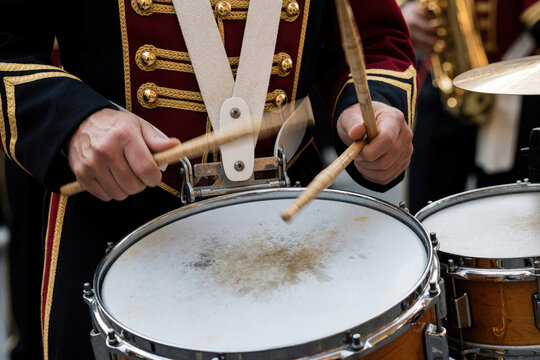Musician in uniform plays snare drum with sticks during outdoor parade. Percussionist creates rhythm, part of marching band or military ensemble.