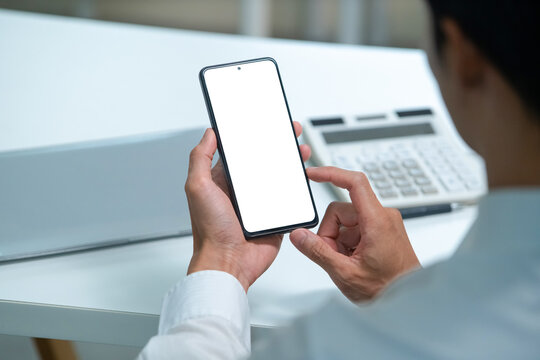 Businessman Holding Smartphone with Blank White Screen Mockup in Office with Calculator on Desk