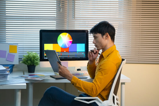 Graphic Designer Reviewing Color Wheel on Monitor While Holding Tablet at Creative Workspace Desk