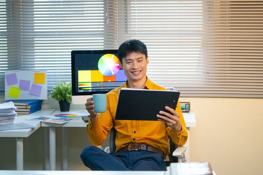 Creative Graphic Designer Reviewing Work on Tablet with Color Wheel on Monitor in Modern Office Workspace