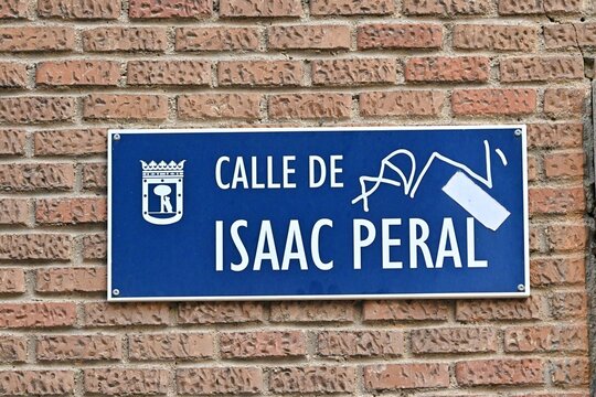 A blue metal street sign reading "Calle de Isaac Peral" in Madrid, Spain, mounted in close-up on a classic red brick facade.August 28, 2026