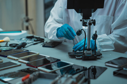 Technician Disassembling Mobile Phone with Precision Tools at Repair Workstation