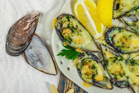 Baked mussels with cheese, herbs, and lemon on a plate, white-sand beach background
