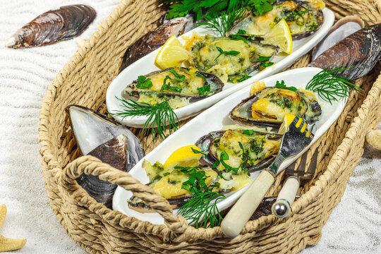 Baked mussels with cheese, herbs, and lemon served in a wicker tray on a sandy background